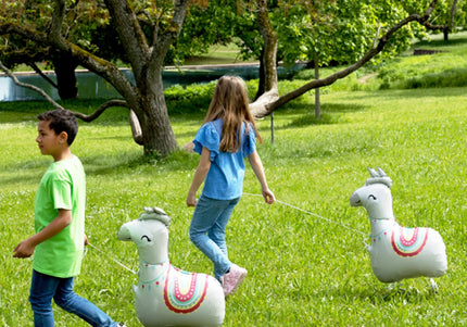 Kinder spielen mit Airwalker Ballons in Form eines Lamas auf einer Wiese