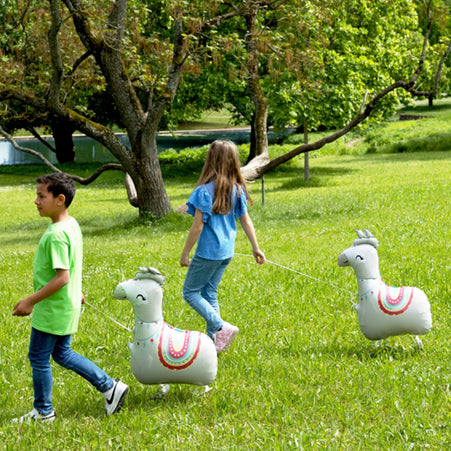 Kinder spielen mit Airwalker Ballons in Form eines Lamas auf einer Wiese